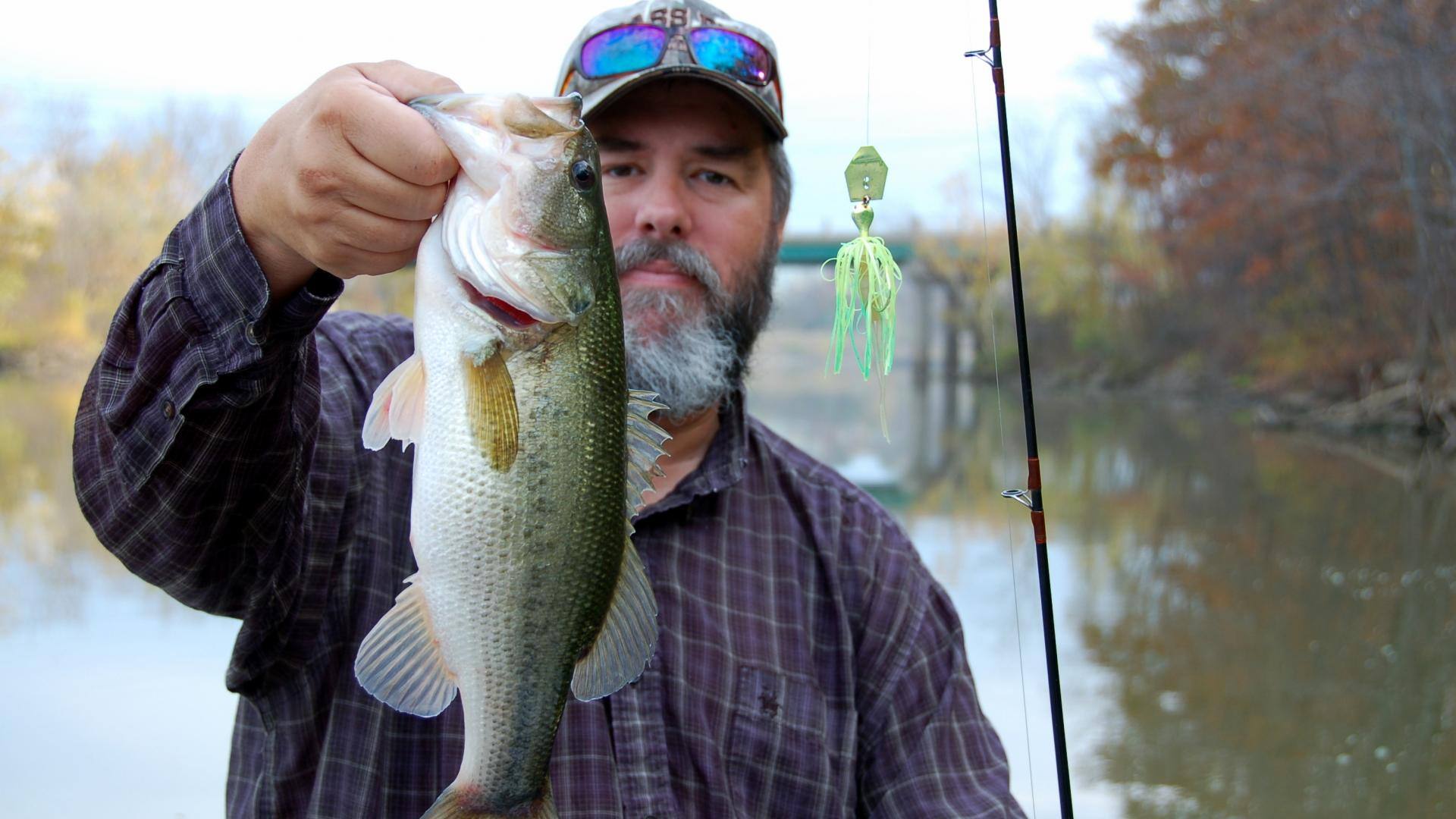 Angler holding a fishing rod in one hand and a largemouth bass in the other 